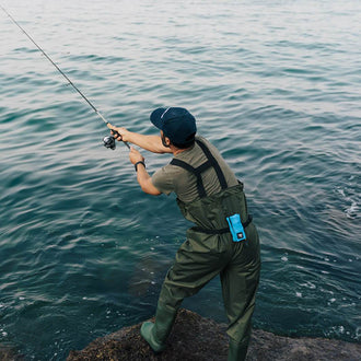 Angler in watt pants standing on rocks with Restube active in ice mint color fishing in dark water