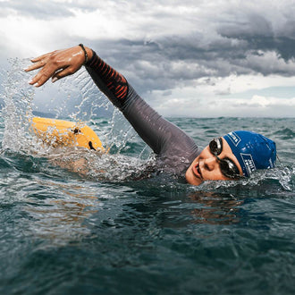 Nathalie Pohl crawls in the sea with swimming goggles, swimming cap and pulls an inflated rest tube swimming buoy behind her
