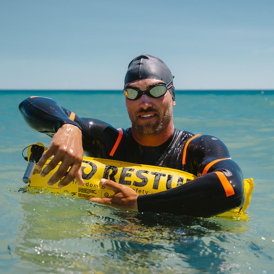 Long distance swimmer in nepren suit with swimming goggles and swimming cap leans over rest tube swimming buoy in sea and rests