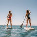 Two female stand up paddlers ride the sea with the added safety of Restube floating buoys