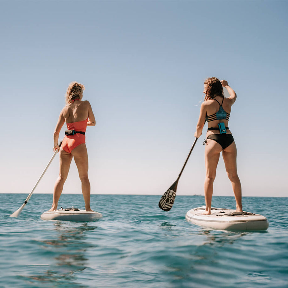 Two female stand up paddlers ride the sea with the added safety of Restube floating buoys