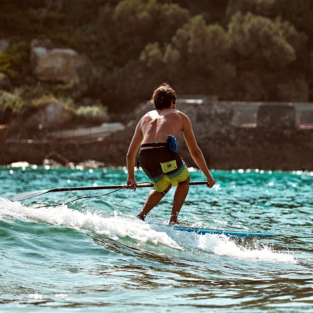 SUP board rider with restube around waist riding a wave in the sea
