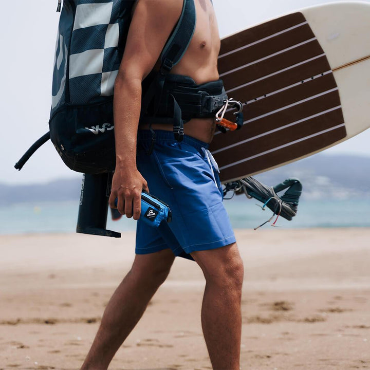 Man with practical small packed restube buoy and kiteboard under arm goes surfing across beach
