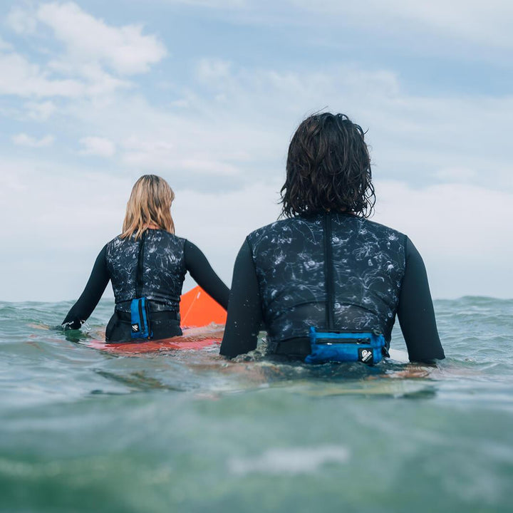 Two surfers wait for waves with Restube extreme sitting on their surfboards